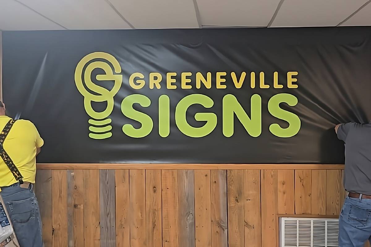 Two professionals installing a custom business logo design on an interior wall with wood paneling near Greeneville, Tennessee (TN)