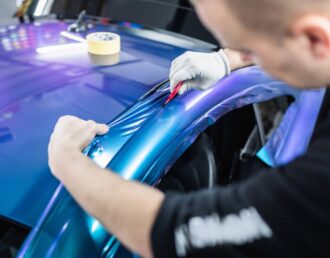 A car wrapping specialist working on a vehicle wrap, placing blue vinyl on the car at Greeneville Signs near Greeneville, TN