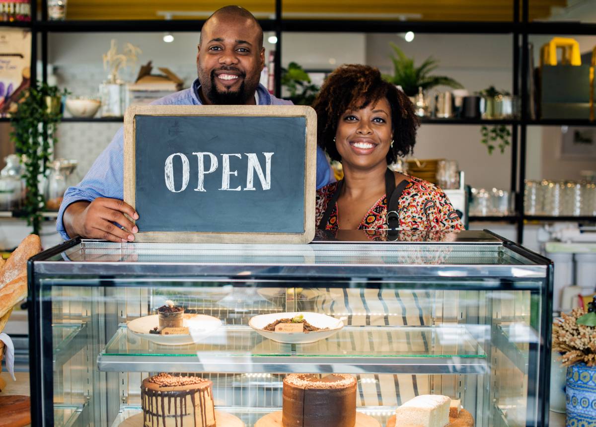 Two local business owners in their newly opened café shop, holding an “Open” sign