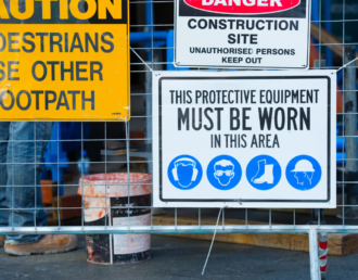 A collection of new construction site signage, with directions for pedestrians and workers, on a fence