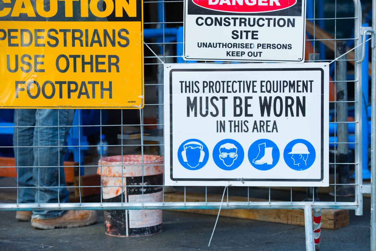 A collection of new construction site signage, with directions for pedestrians and workers, on a fence