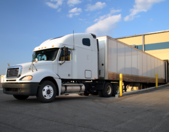 A white semi-truck, lacking truck wraps or truck door decals, backed into a loading dock